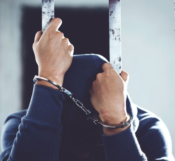 Handcuffed hands of a prisoner behind the bars of a prison with blue clothes
